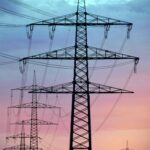 Electricity pylons silhouetted against a dramatic sunset sky, showcasing high voltage transmission.